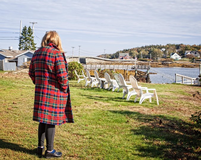 A young woman stands looking out at the water in Maine.