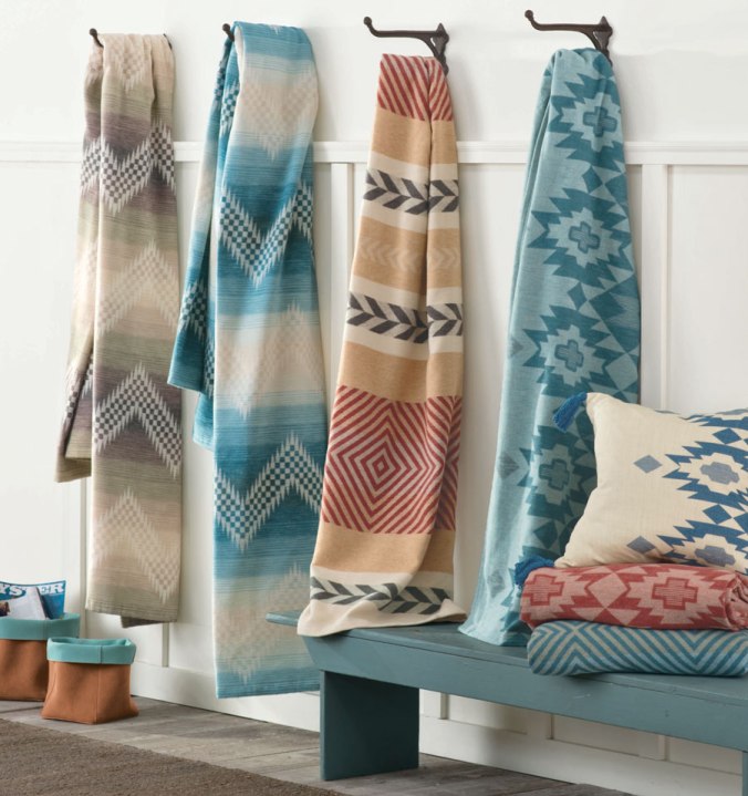 Four Pendleton cotton bed blankets hang on hooks against a white wall. 