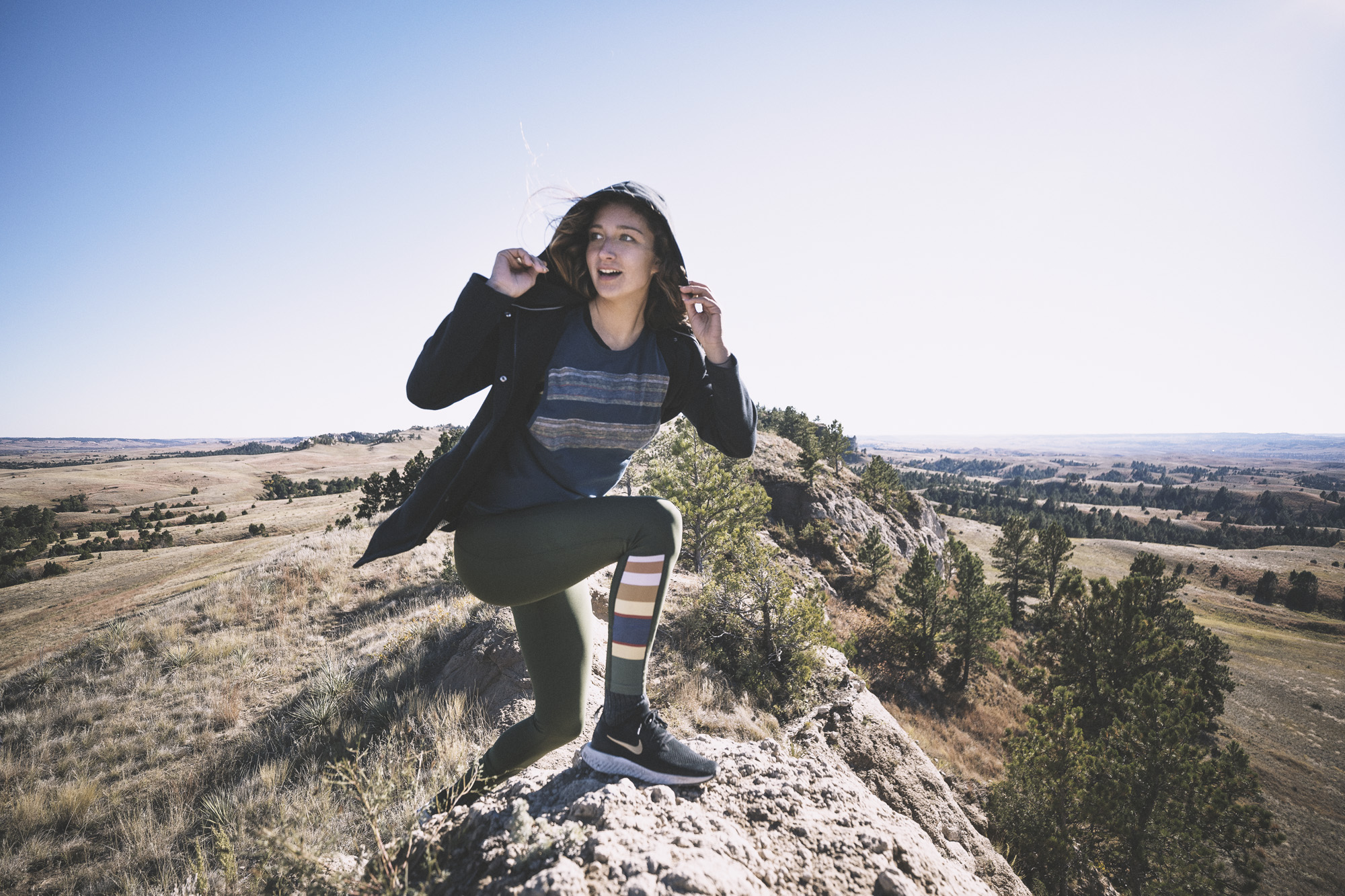 A young woman stands on top of a rocky ridge in the sunshine, wearing Pendleton x Hurley activewear.
