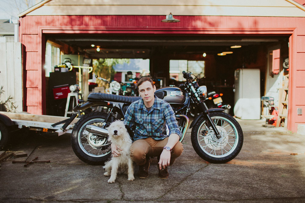 A man kneels in his driveway in front of a motorcycle, with is arm around a white fluffy dog. he is wearing a Pendleton Board Shirt in Original Surf Plaid.