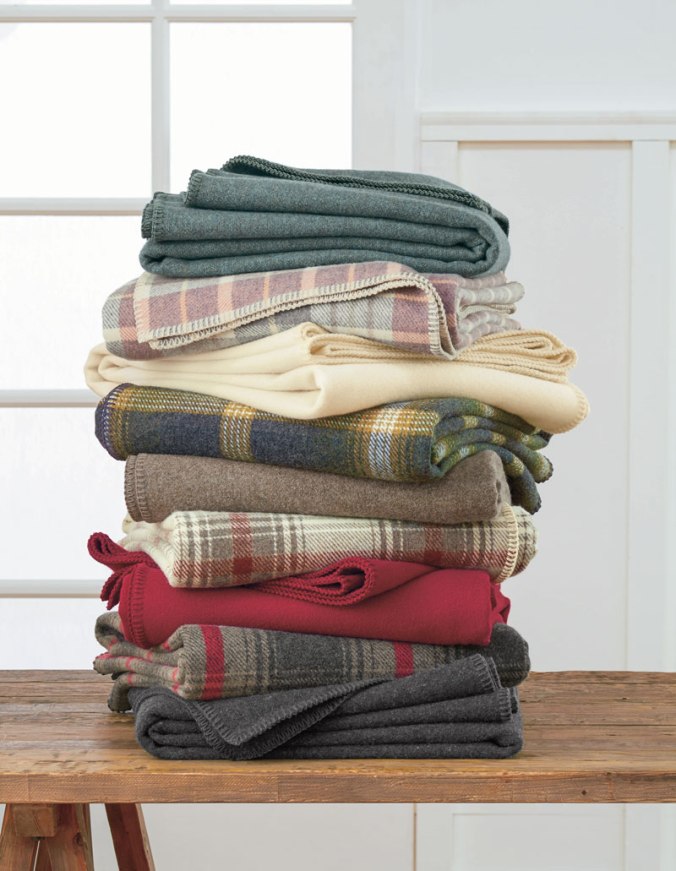 A stack of folded Pendleton Eco-Wise Wool bed blankets on a wooden table.